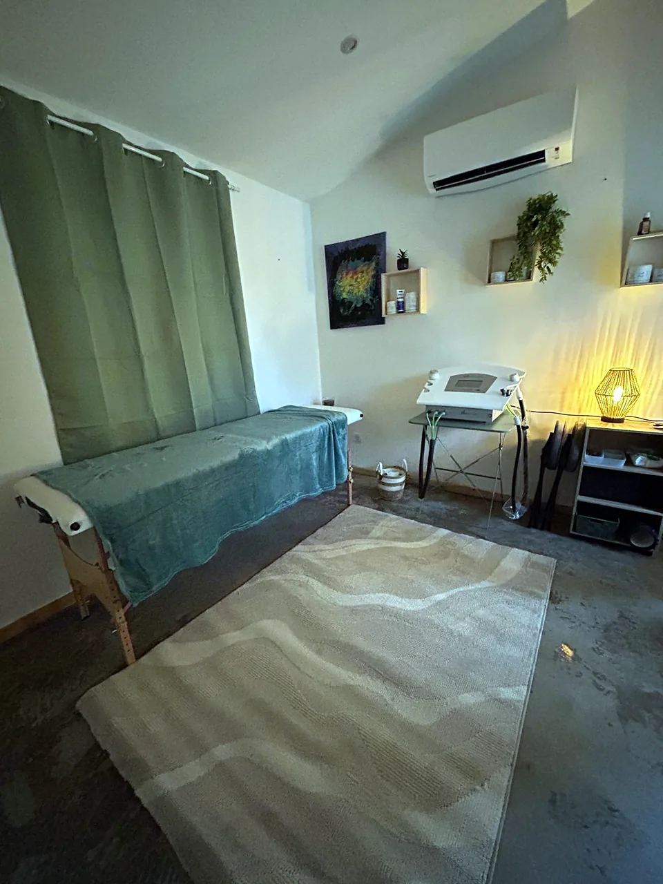 La table de soins sous un plaid vert, devant un rideau vert, et l’appareil de cryothérapie près de la lampe