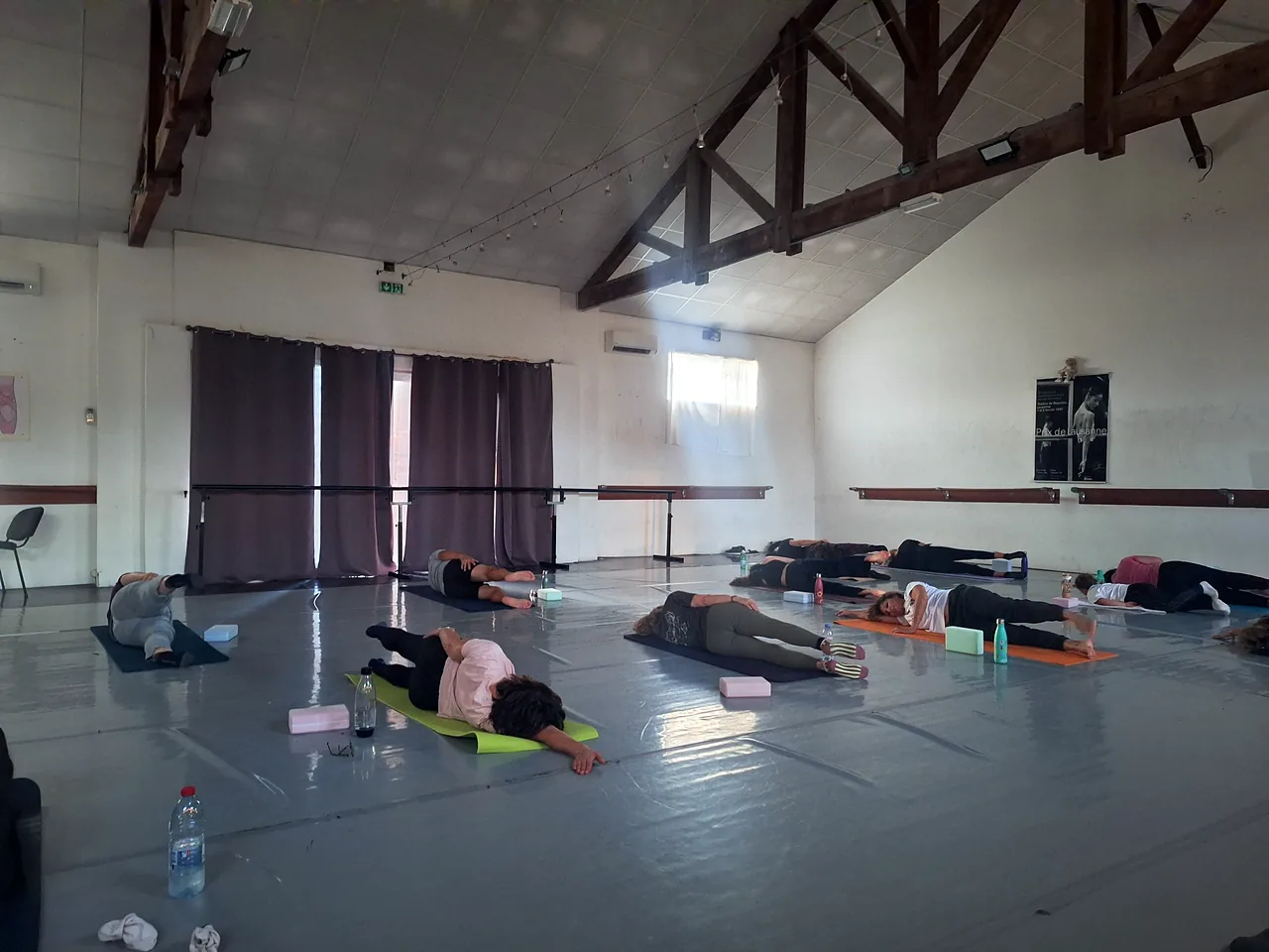Un cours de pilates au studio de danse : une dizaine d’élèves allongées sur le côté, sur leurs tapis, sous une charpente en bois